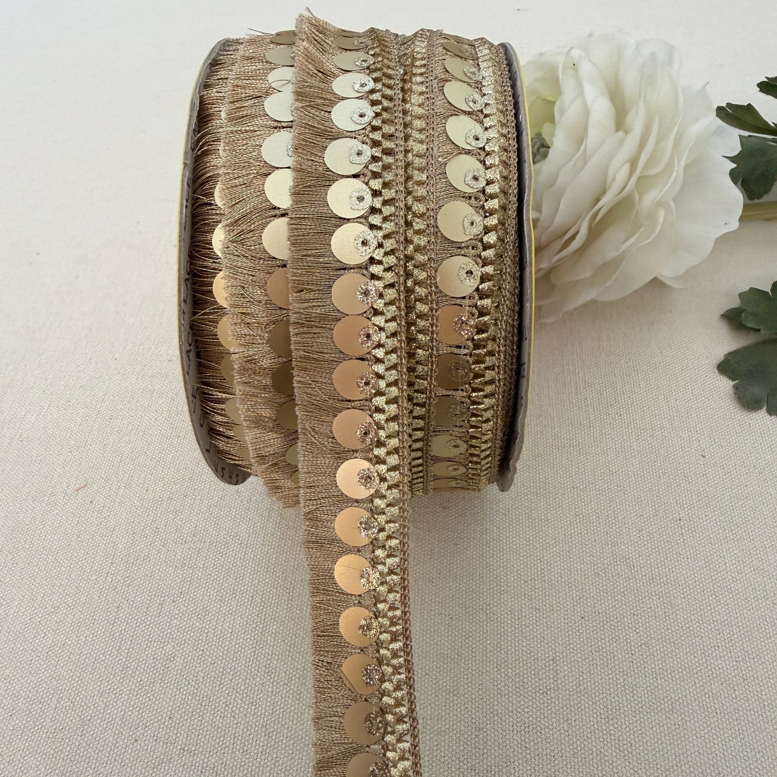 Decorative ribbon with gold sequins and fringe on a neutral background