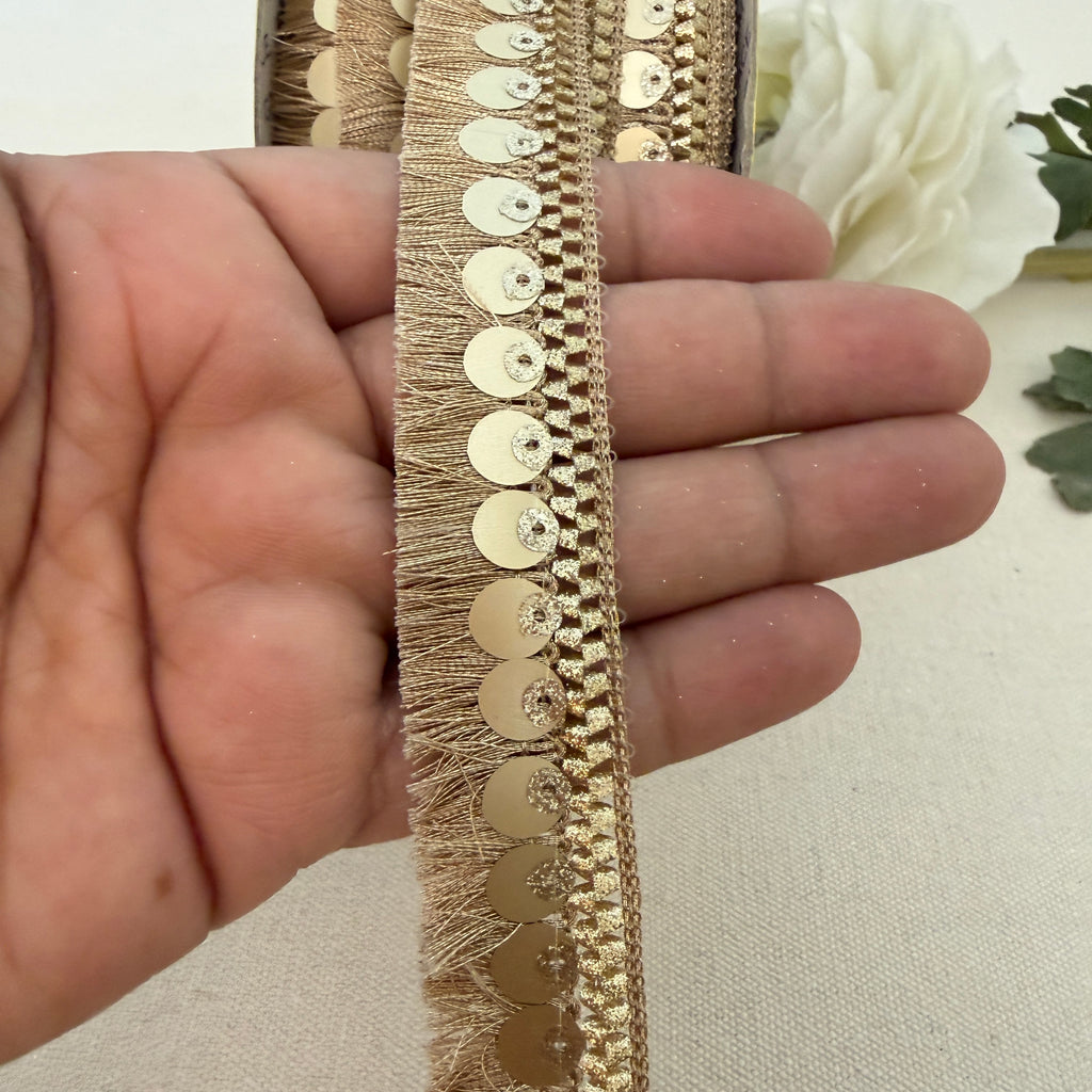 Gold lace trim held between fingers with a white flower in the background