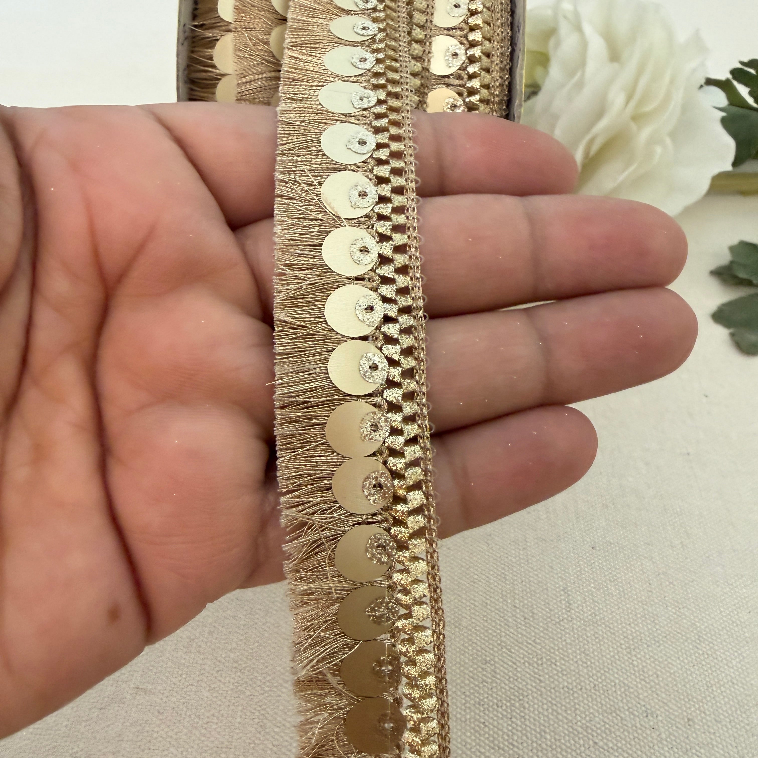 Gold lace trim held between fingers with a white flower in the background