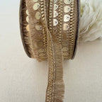 Close-up of a spool of decorative ribbon with fringe and sequins on a light background.