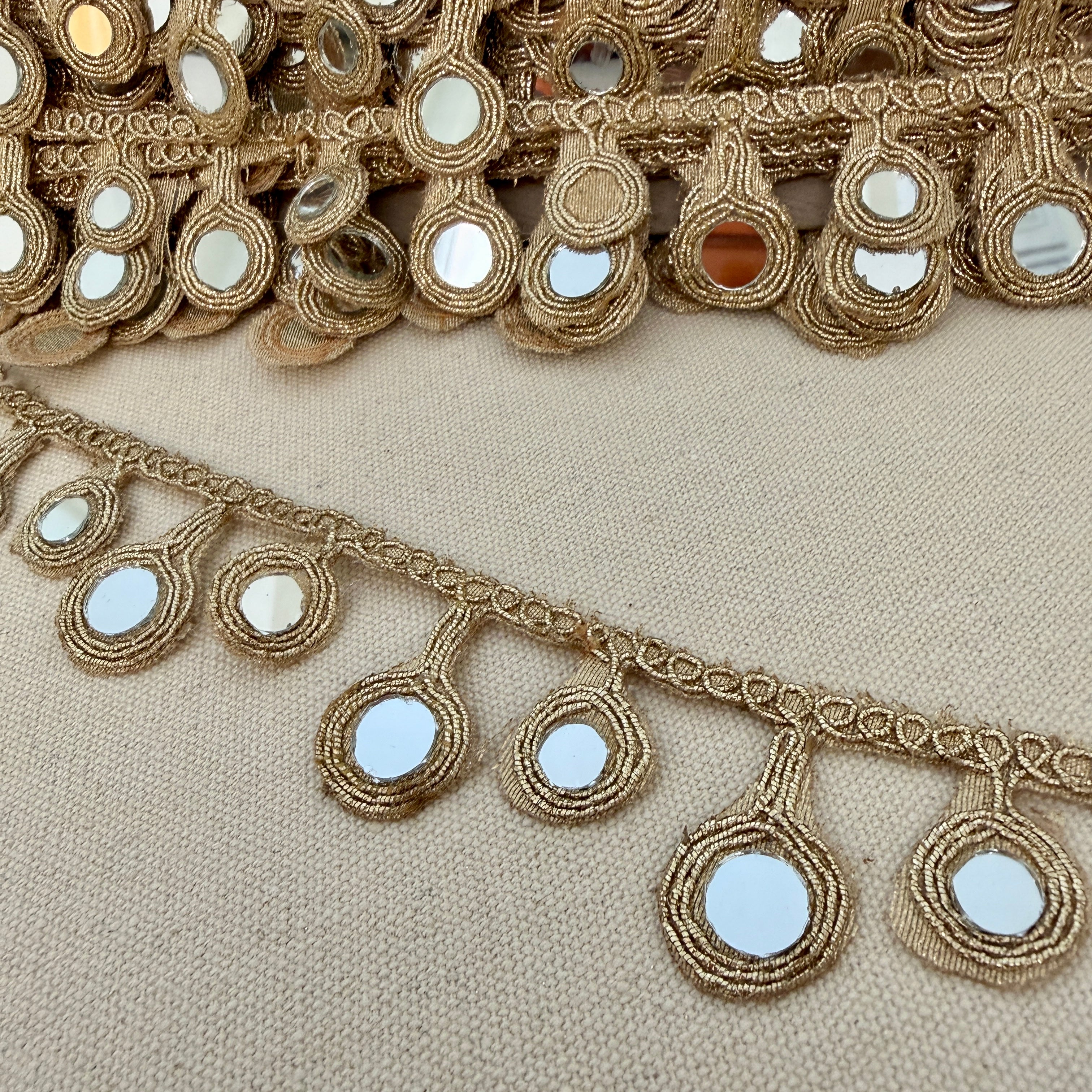 Decorative gold trim with mirror embellishments on a beige fabric background