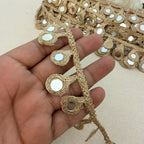 Decorative gold fabric trim held by a hand on a beige background