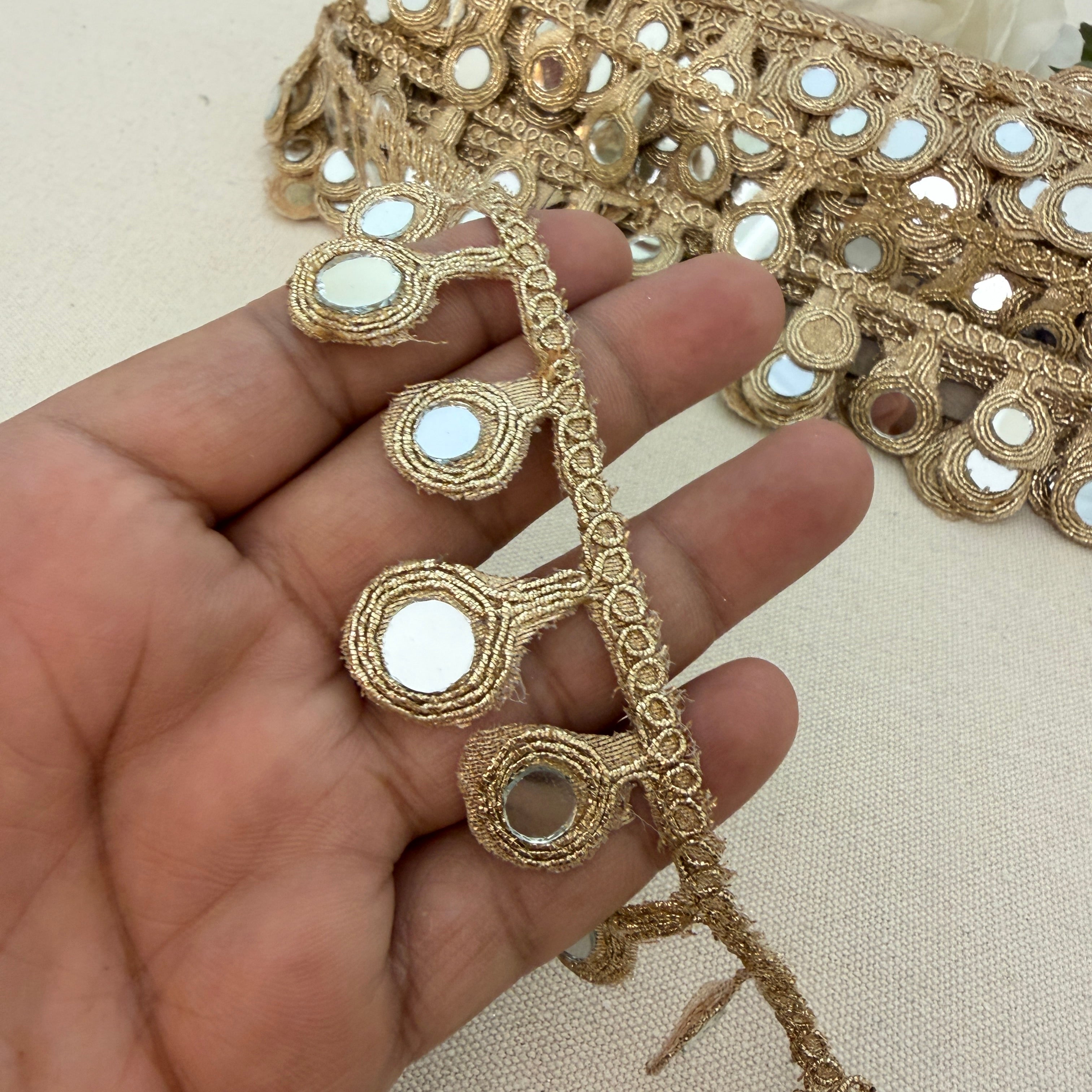 Decorative gold fabric trim held by a hand on a beige background