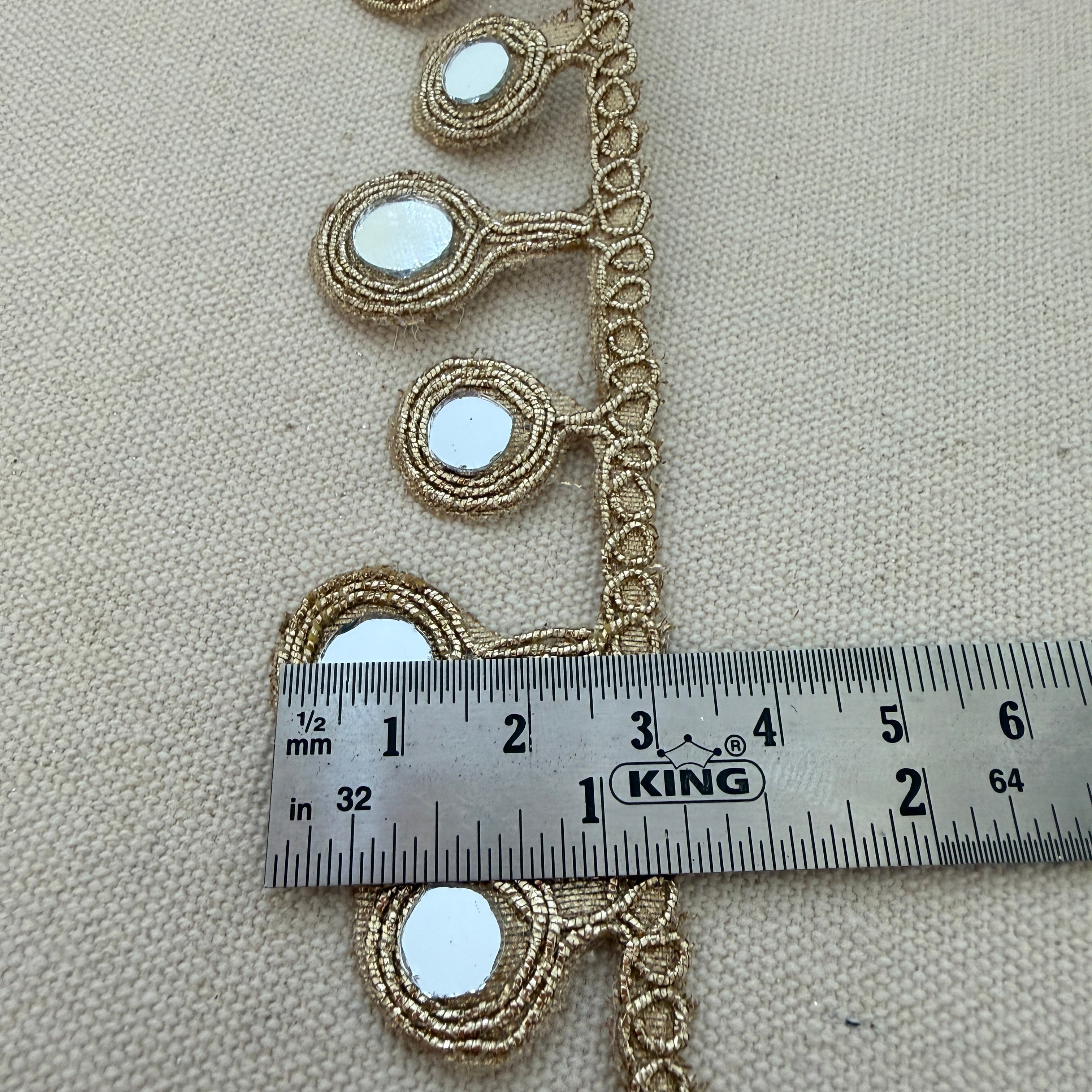 Decorative gold lace with a ruler for scale on a beige background