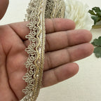 Gold lace trim held between fingers with a white flower in the background