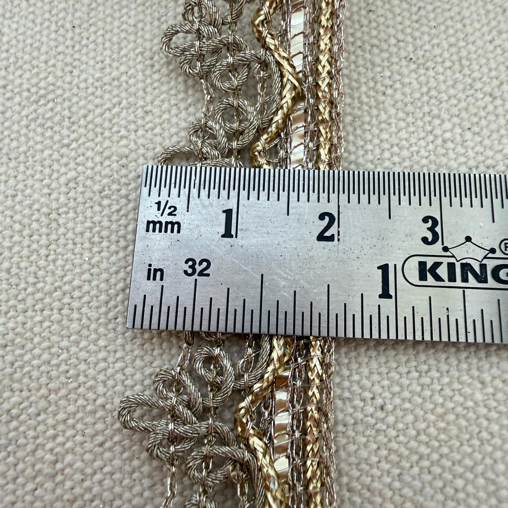 Three gold chains draped over a ruler on a textured beige background