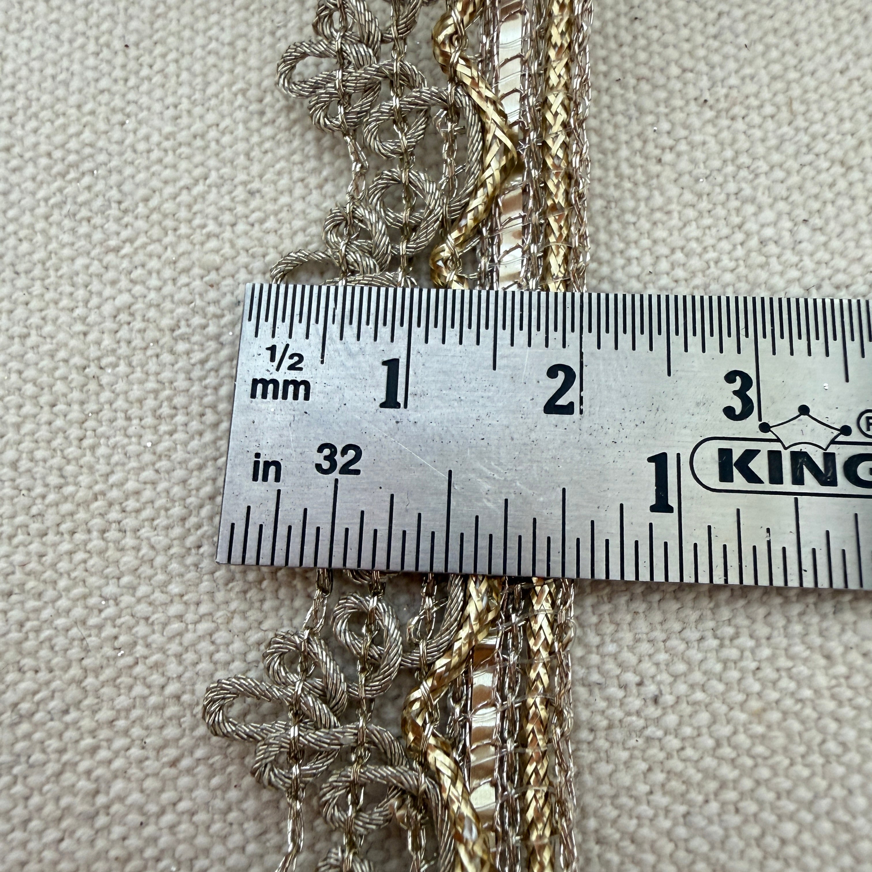 Three gold chains draped over a ruler on a textured beige background