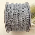 Spool of silver lace fabric on a beige background