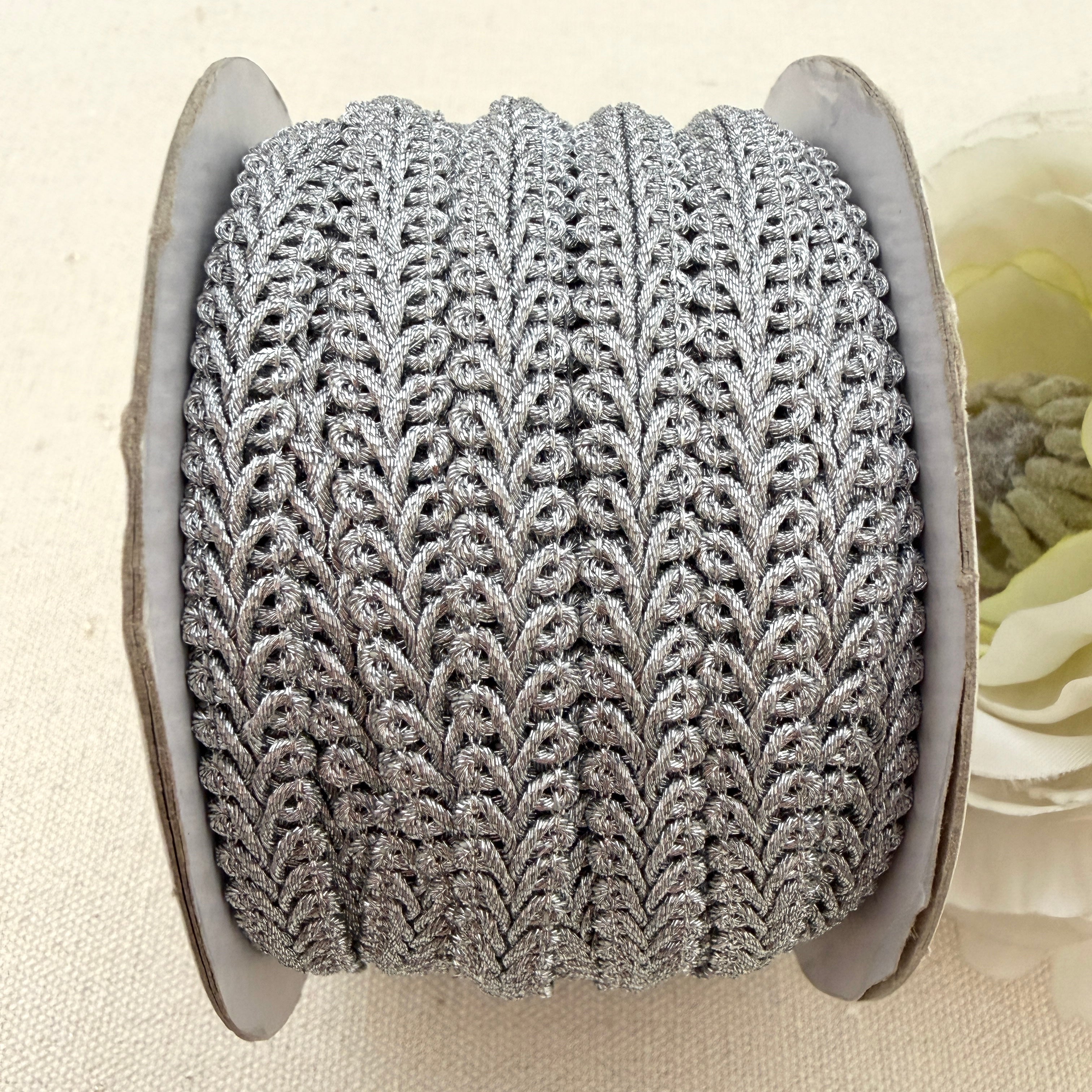 Spool of silver lace fabric on a beige background