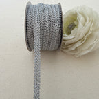 Spool of decorative lace ribbon with a white flower on a beige background