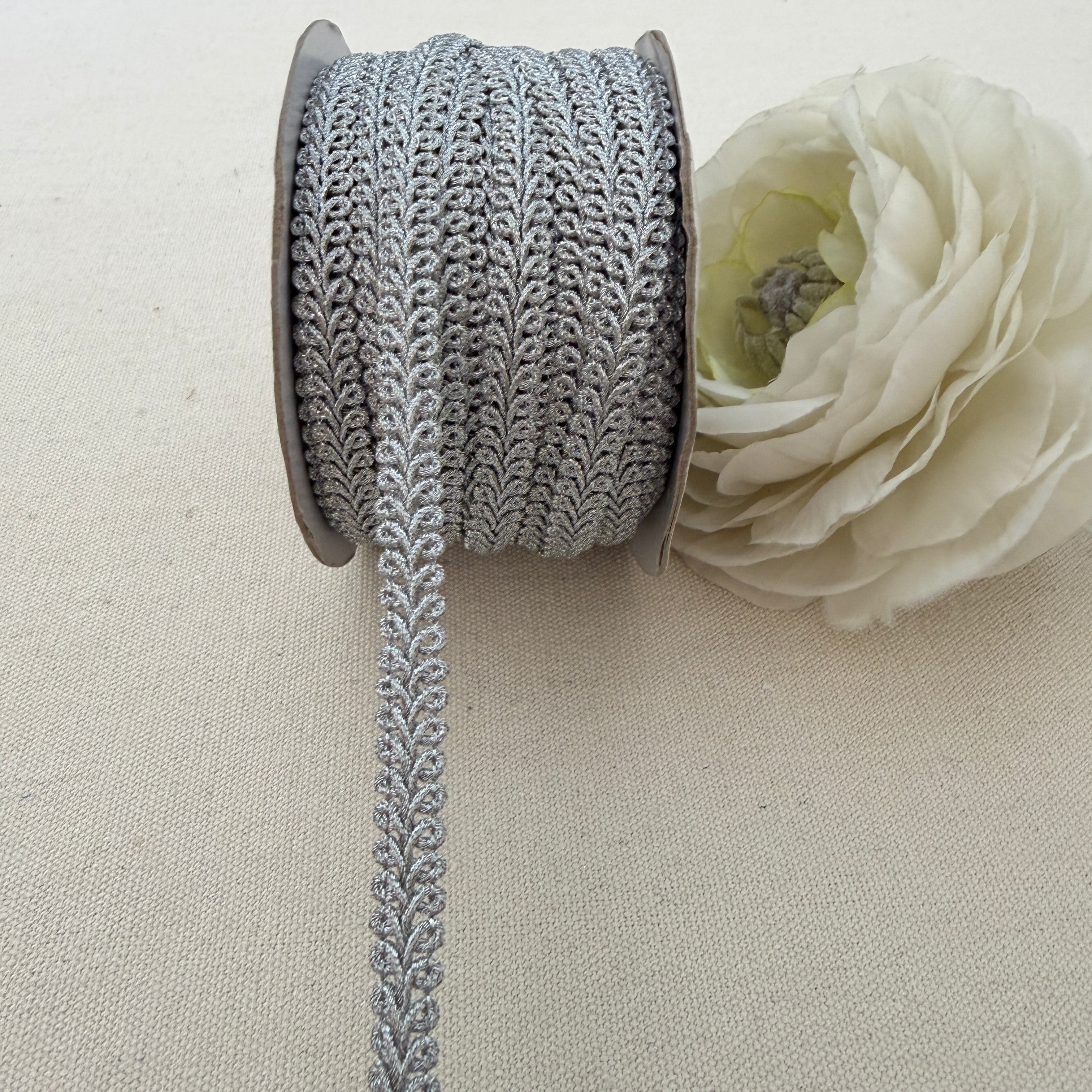 Spool of decorative lace ribbon with a white flower on a beige background