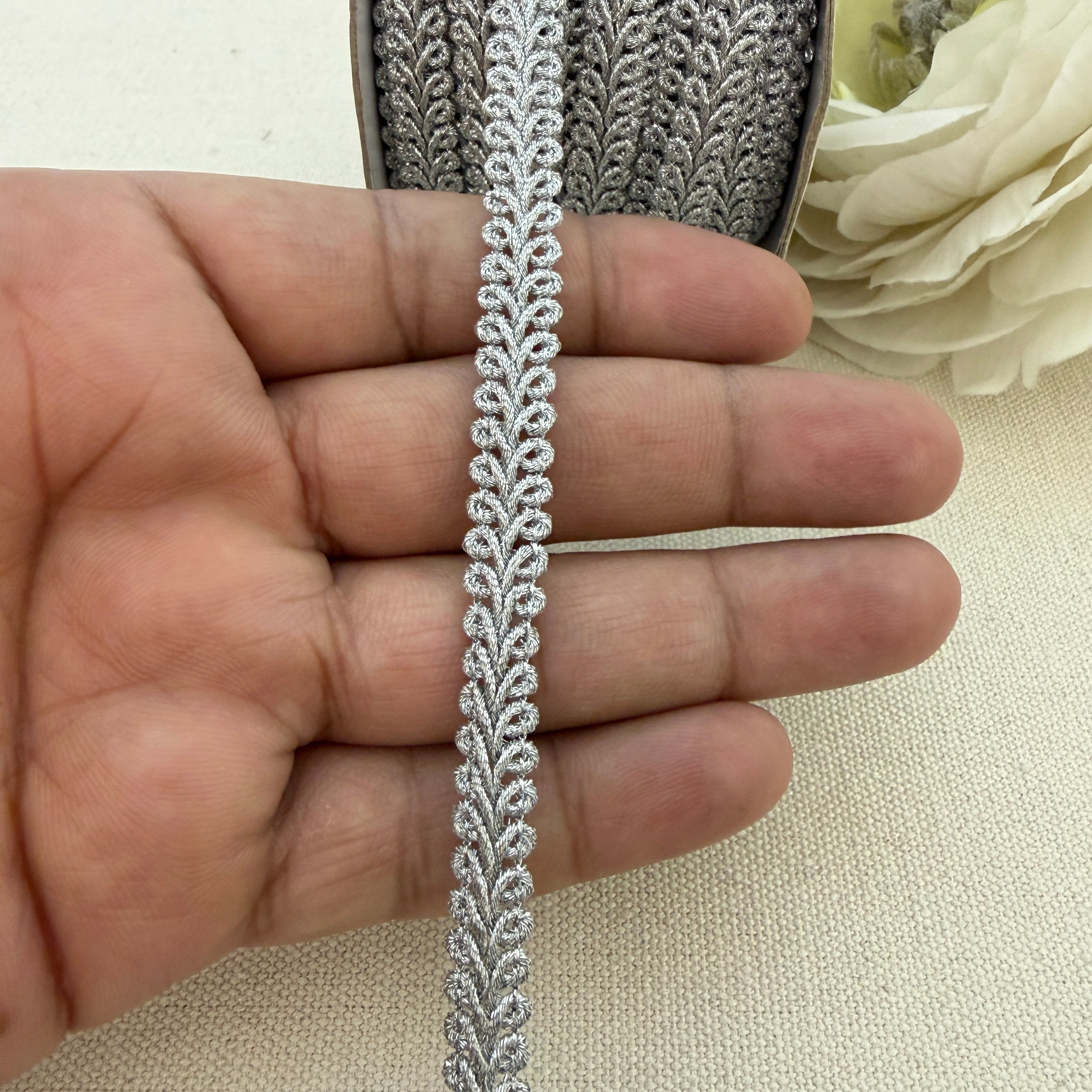 Close-up of decorative lace trim held between fingers with a floral background