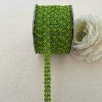 Green lace ribbon spool with a white flower on a beige background