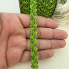 Green decorative trim held between fingers with a white flower in the background