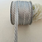 Spool of gray ribbon with a white flower on a beige background