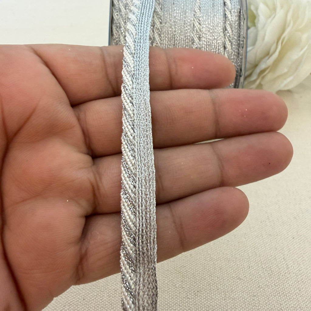 Hand holding a strip of silver metallic ribbon with a blurred floral background