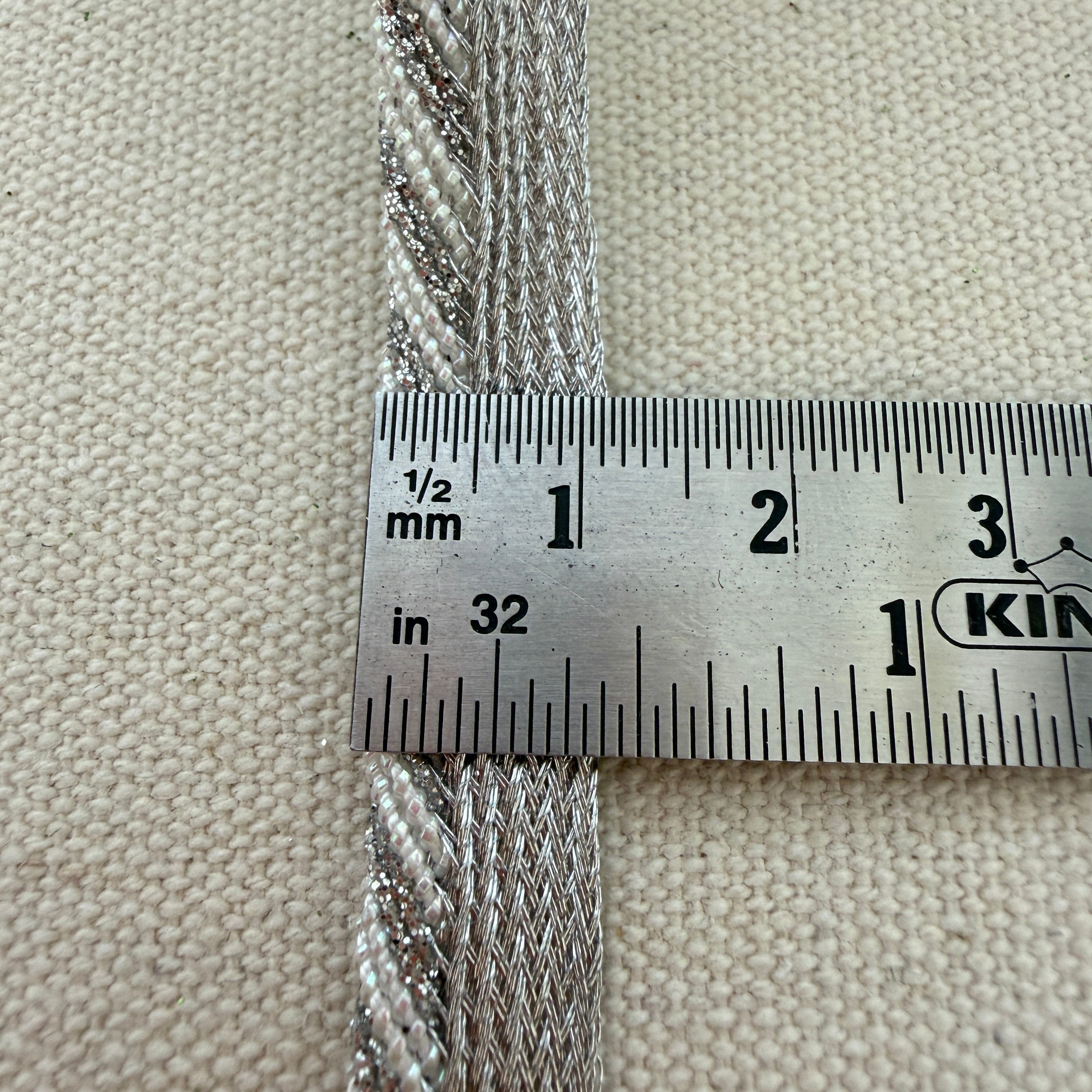 Metallic rope with a ruler showing measurements on a beige fabric background