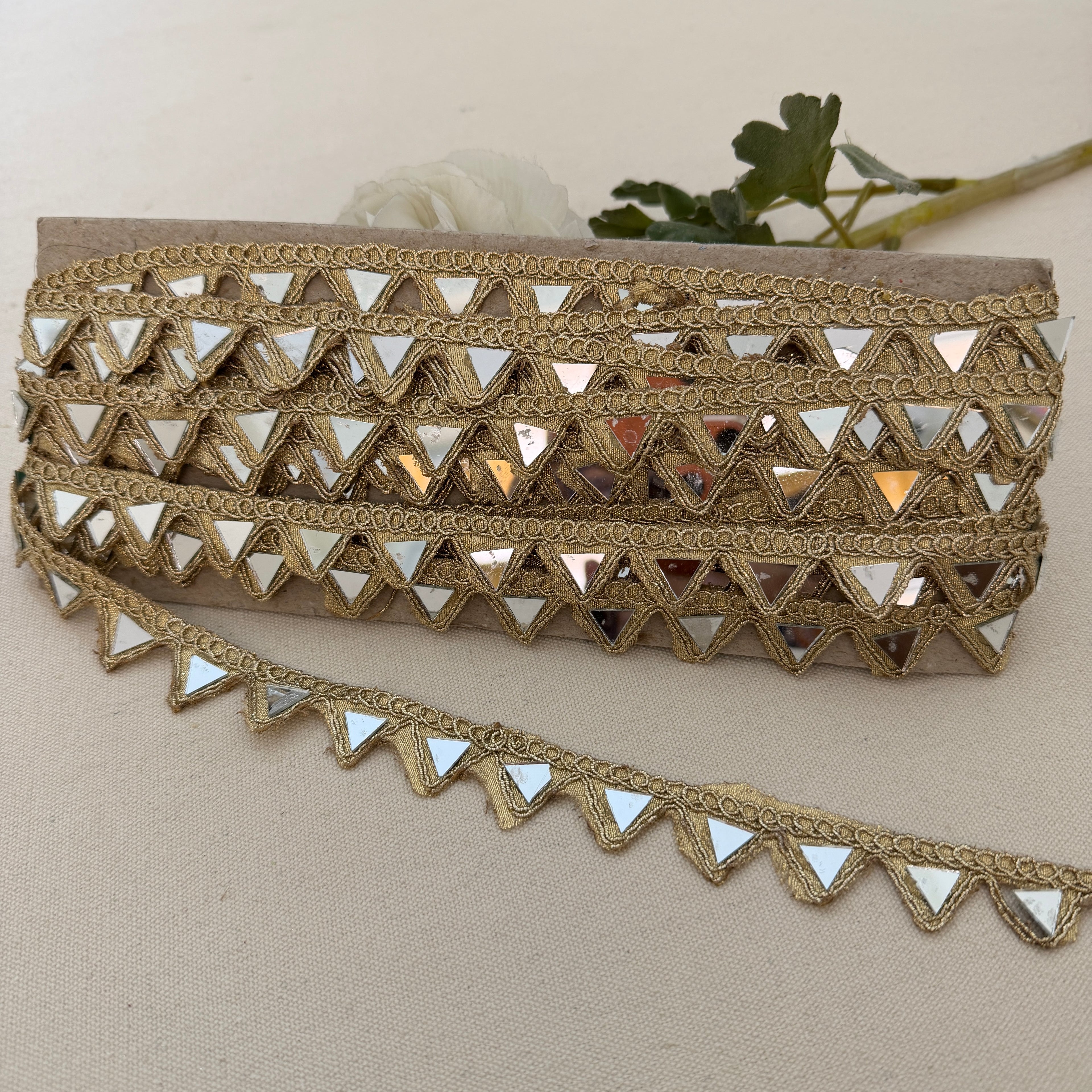 Gold lace trim with mirror-like triangles on a beige background
