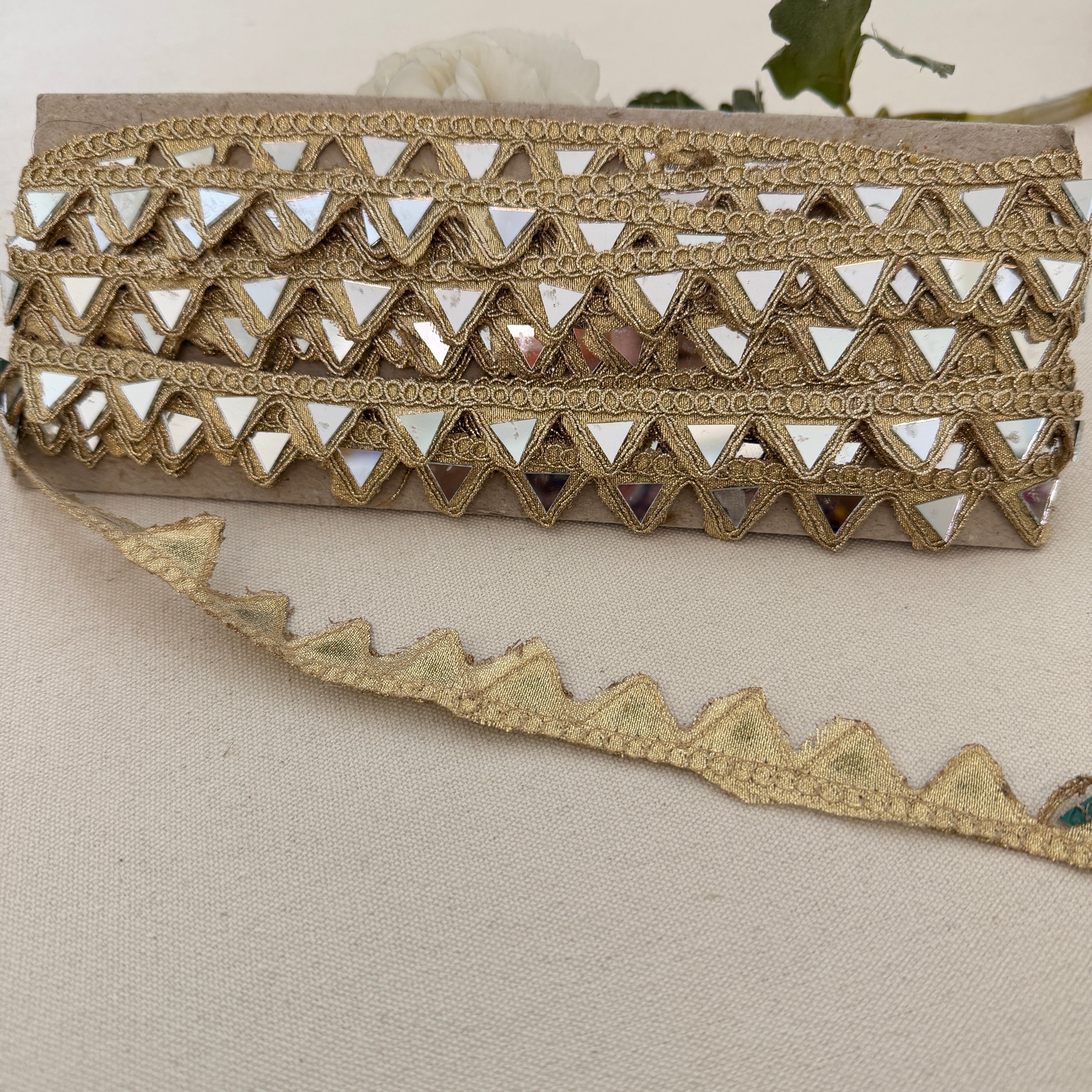 Gold embroidered clutch bag with intricate patterns on a beige fabric background