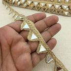 Decorative gold lace strip held between fingers on a beige background