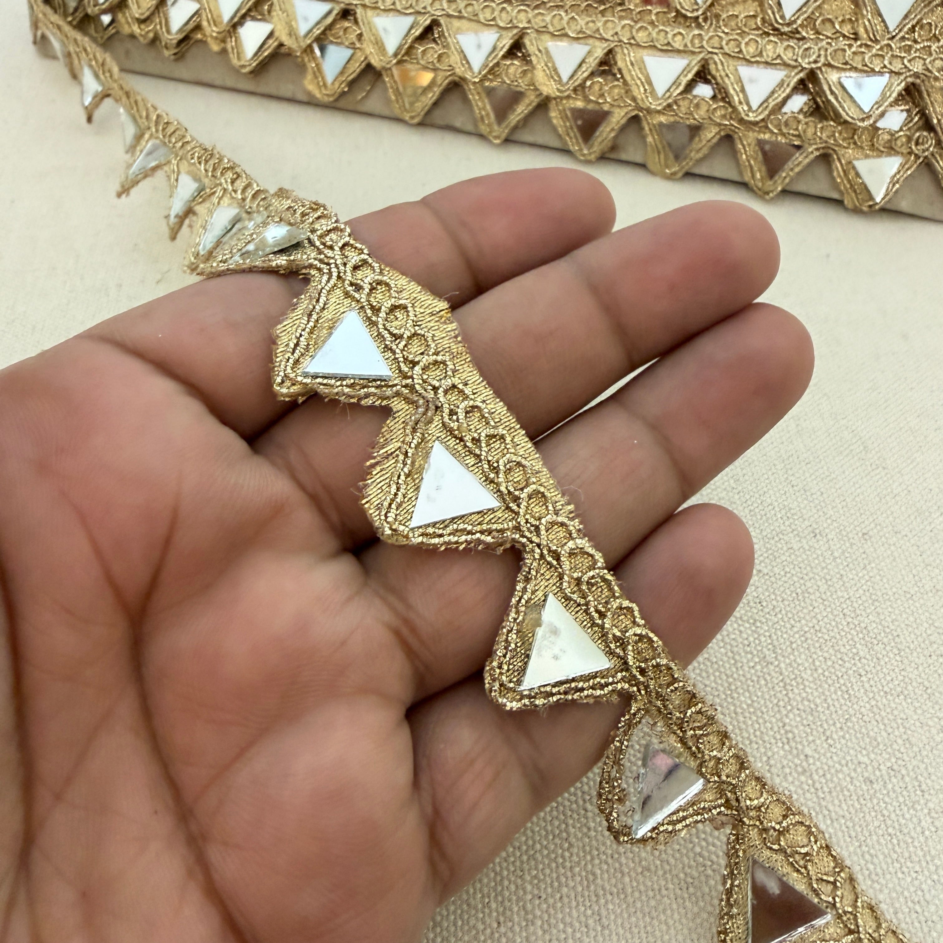 Decorative gold lace strip held between fingers on a beige background