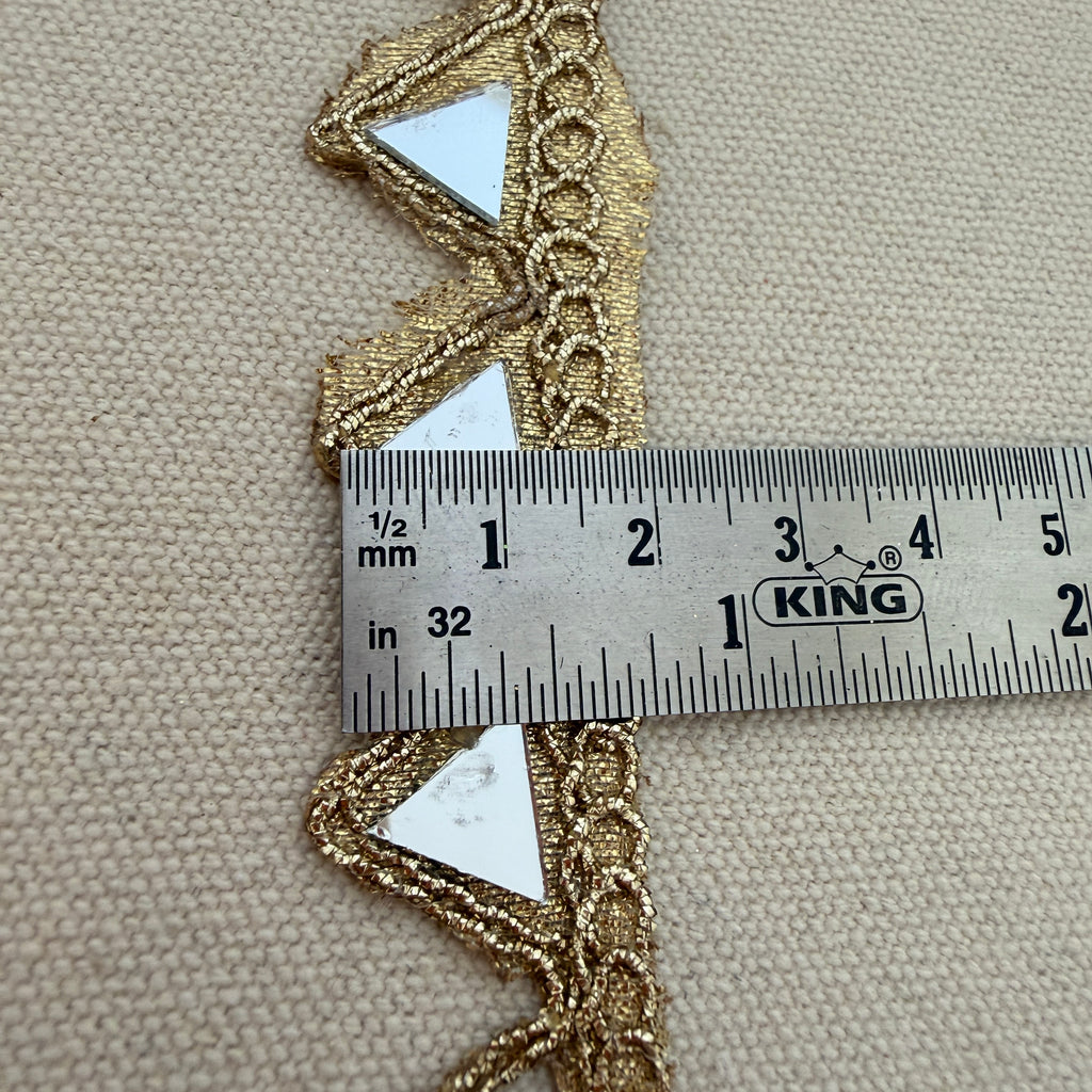 Gold lace trim with a ruler for scale on a beige fabric background