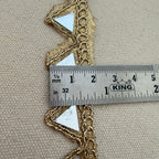 Gold lace trim with a ruler for scale on a beige fabric background