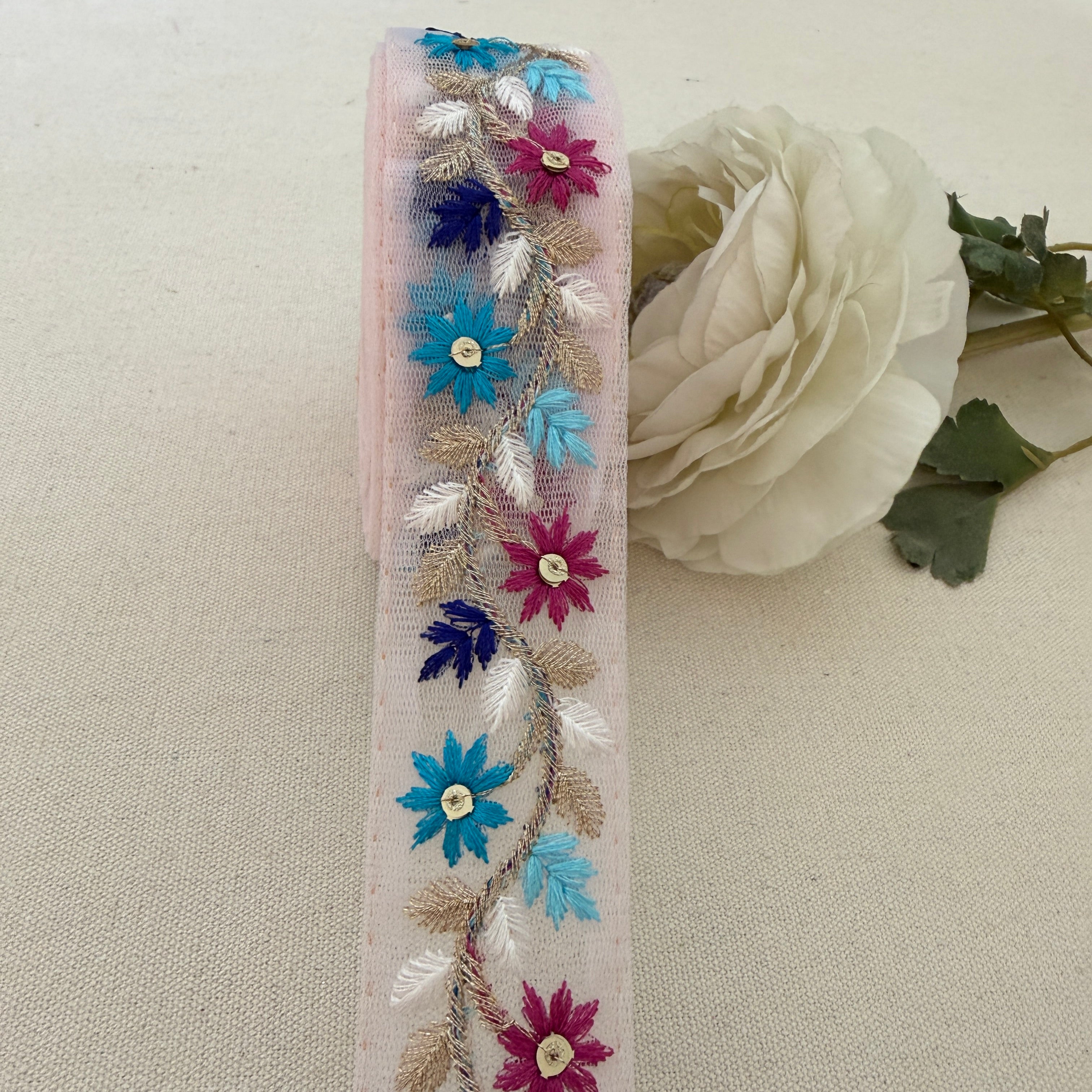 Decorative ribbon with floral embroidery next to a white rose on a beige background