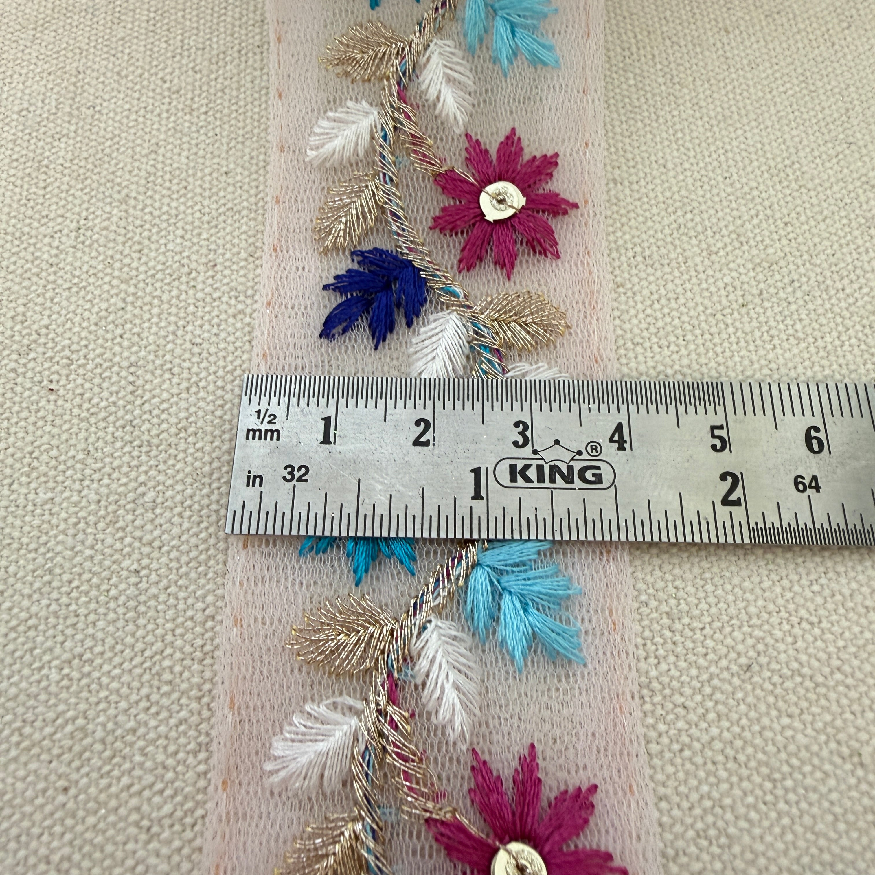 Decorative fabric strip with flowers and leaves measured against a ruler on a beige background