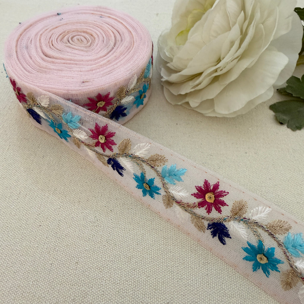 Roll of floral embroidered ribbon with a white flower on a beige background