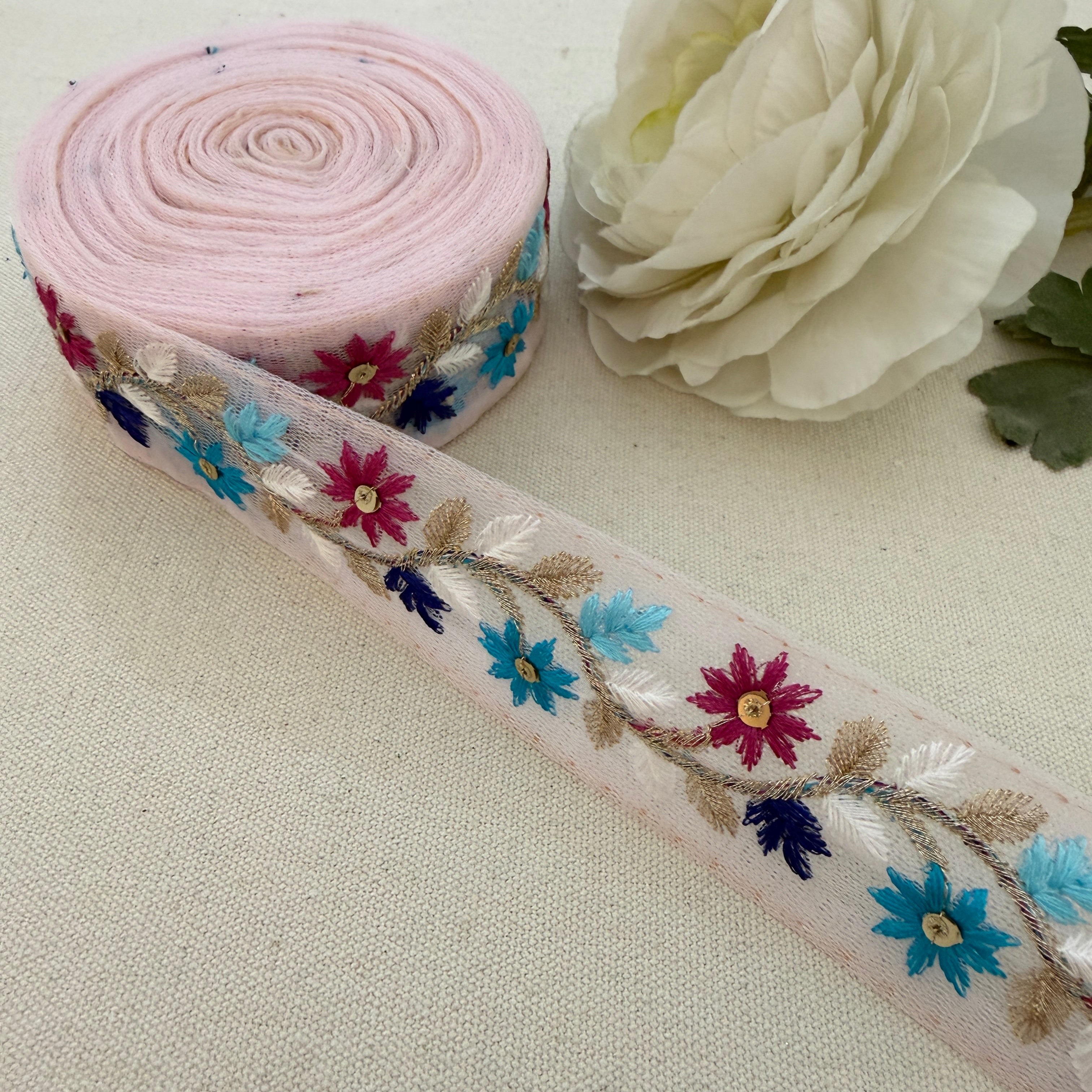 Roll of floral embroidered ribbon with a white flower on a beige background