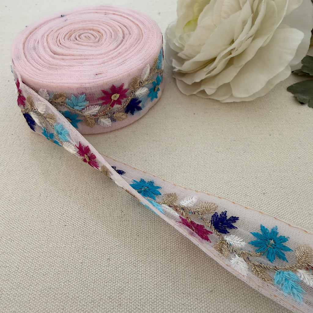 Roll of floral lace ribbon with a white flower on a beige background