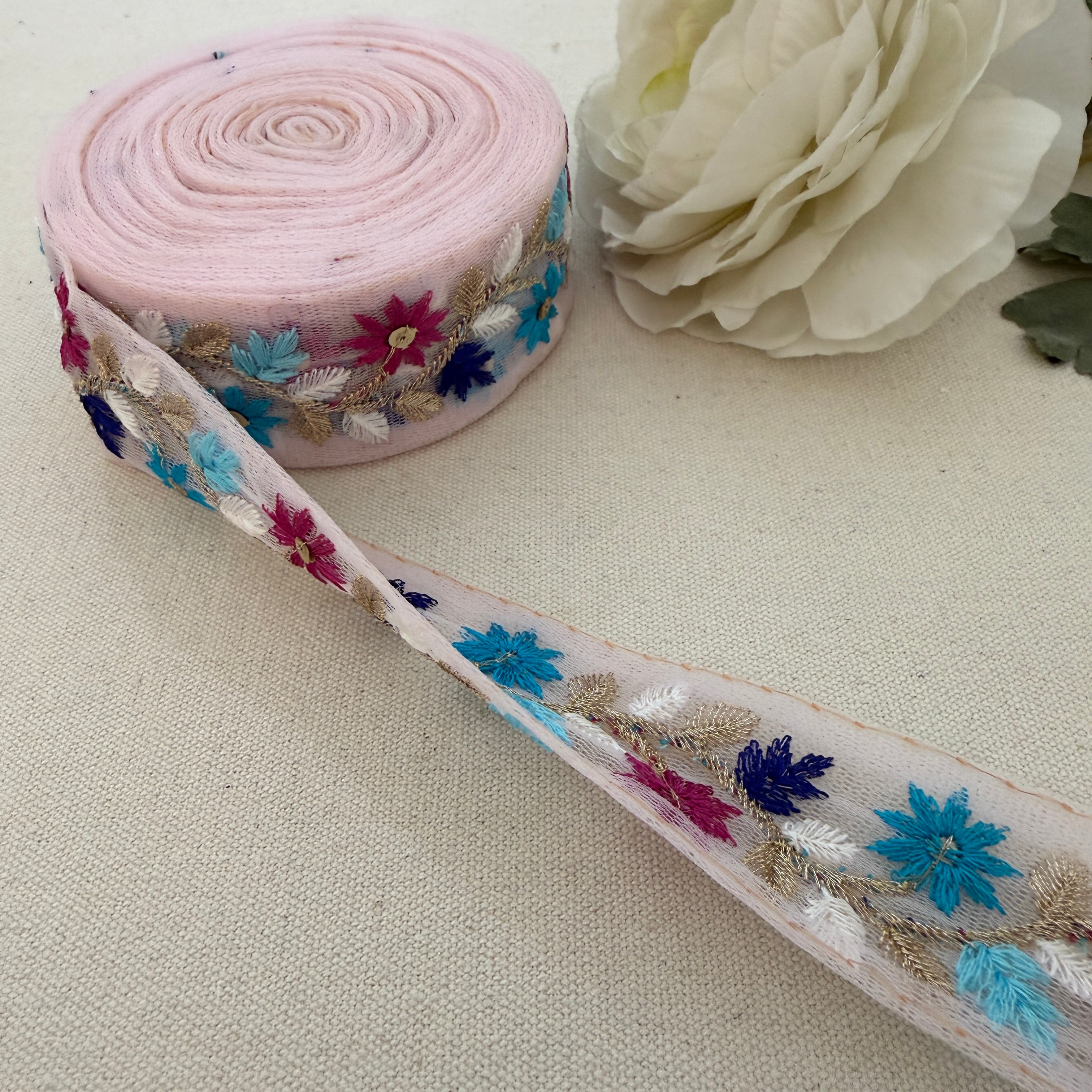 Roll of floral lace ribbon with a white flower on a beige background