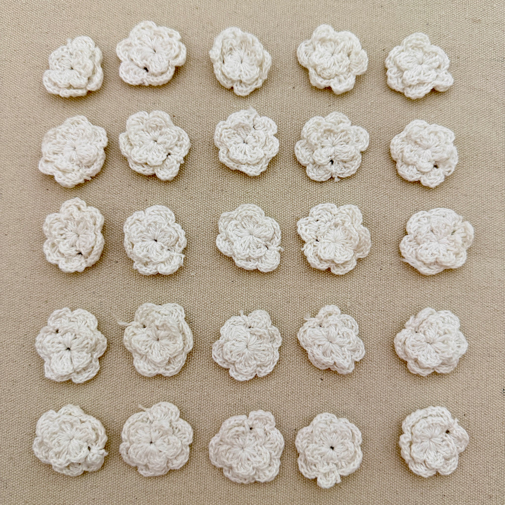 Pattern of white crocheted flowers on a beige fabric background