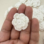 White crocheted flower held between fingers with a beige background