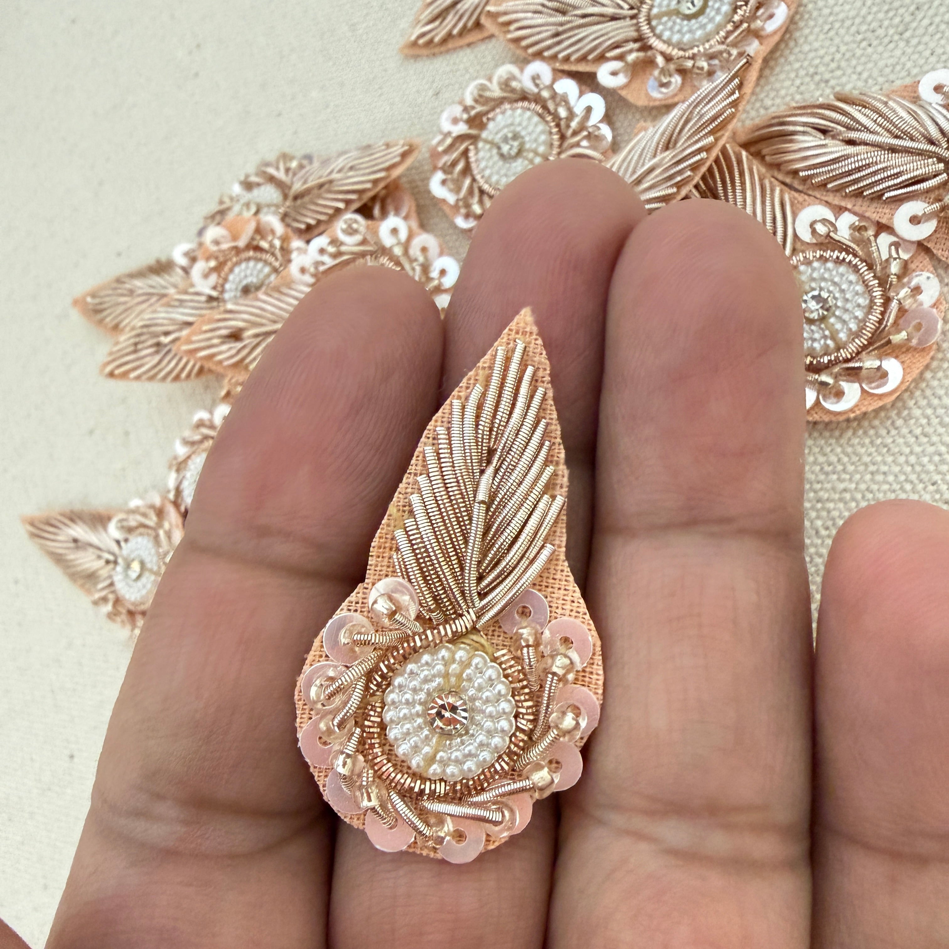 Decorative rose gold and white embroidered patch on a hand with a beige background