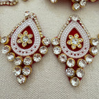 Ornate earrings with red, white, and gold colors on a textured beige background