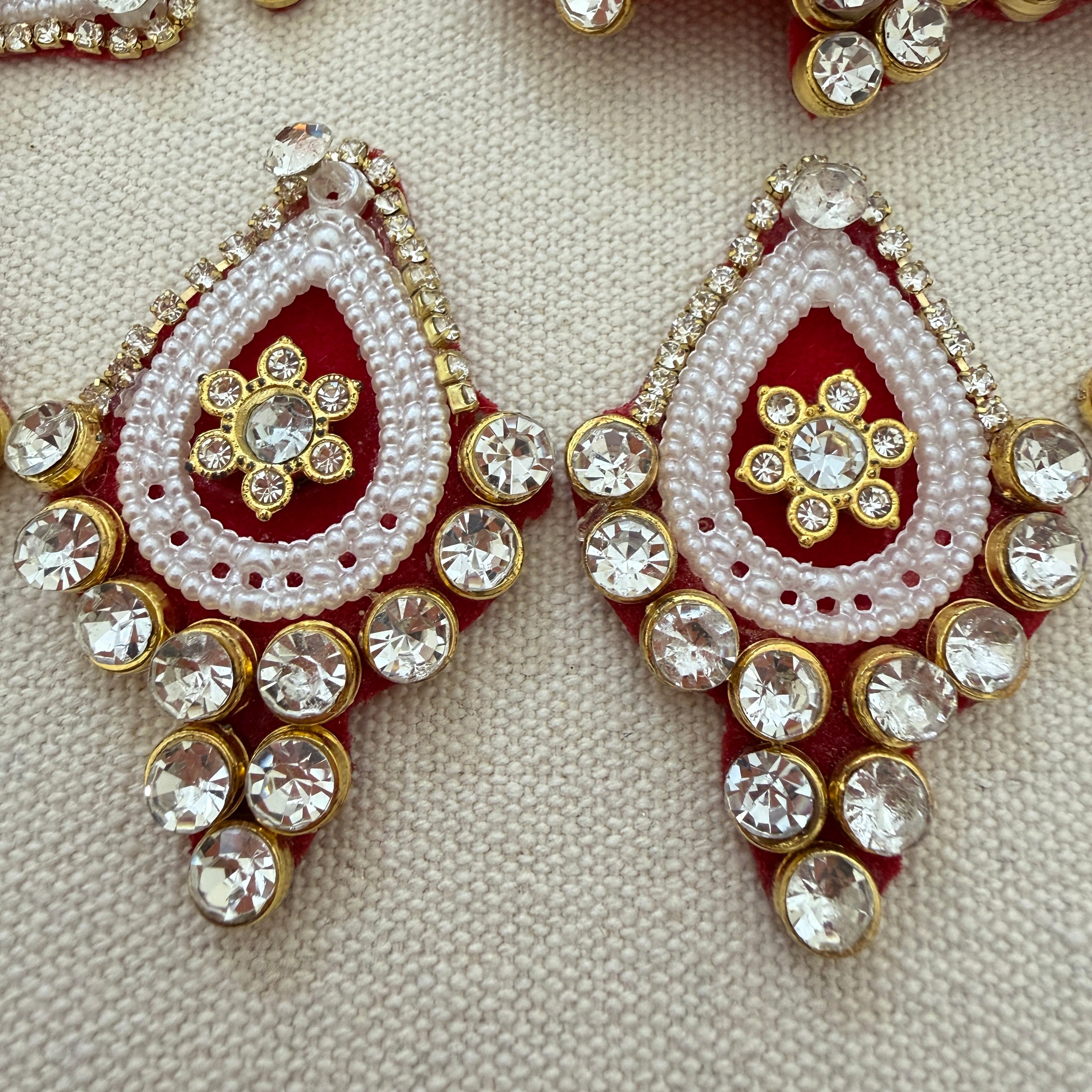 Ornate earrings with red, white, and gold colors on a textured beige background