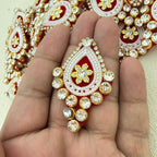 Decorative red and gold jewelry piece held in a hand with a blurred background