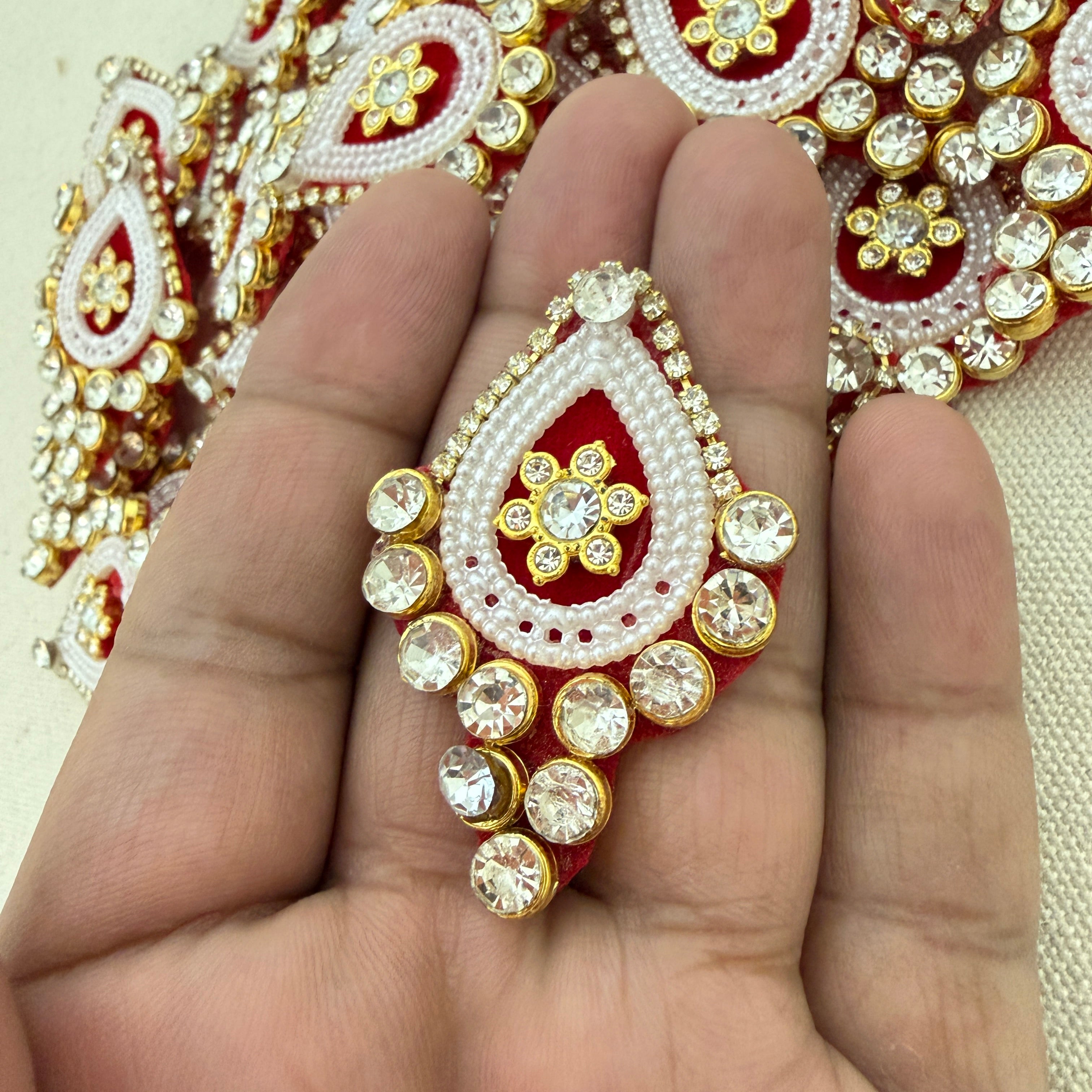 Decorative red and gold jewelry piece held in a hand with a blurred background