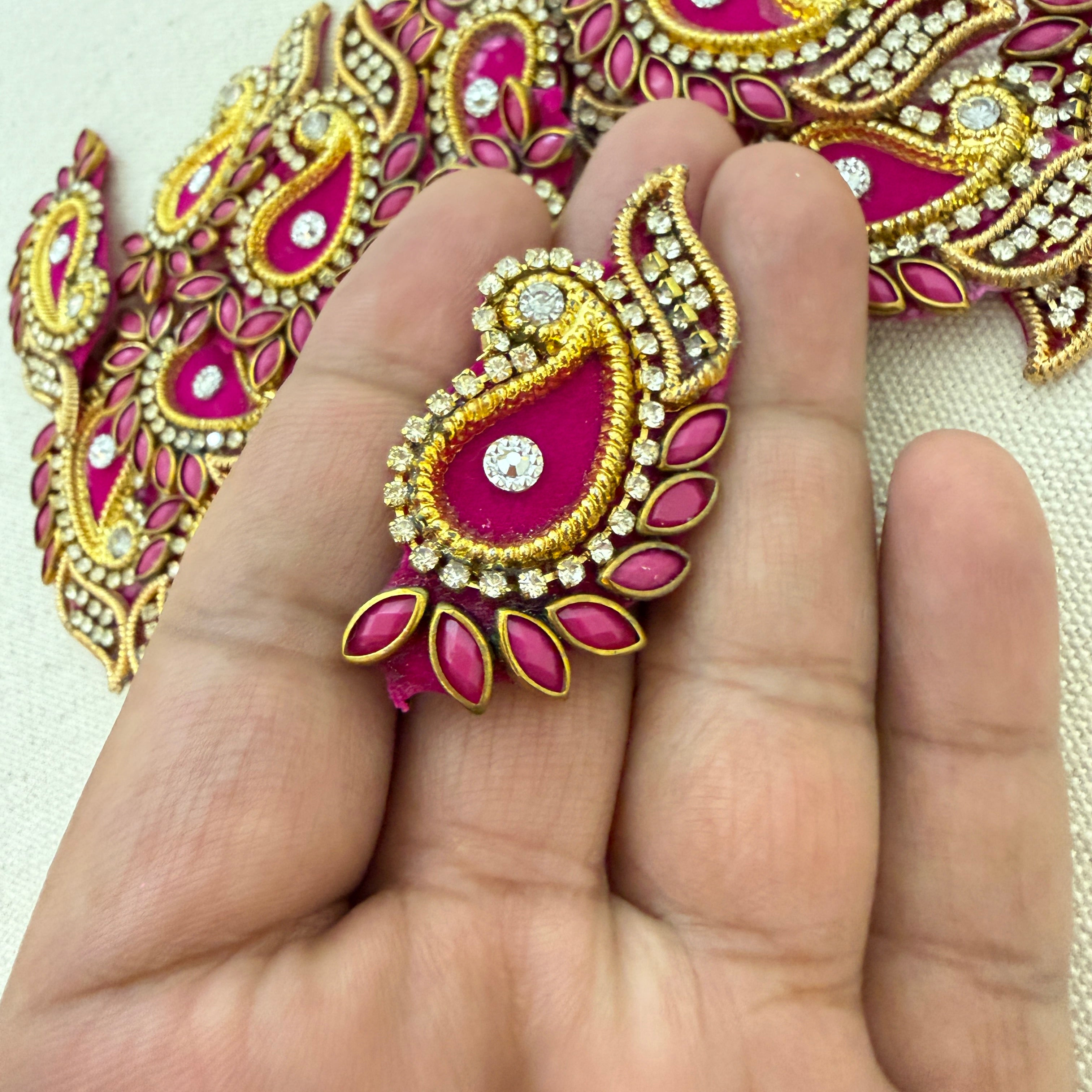 Decorative pink and gold embellishment on a hand with a matching background.