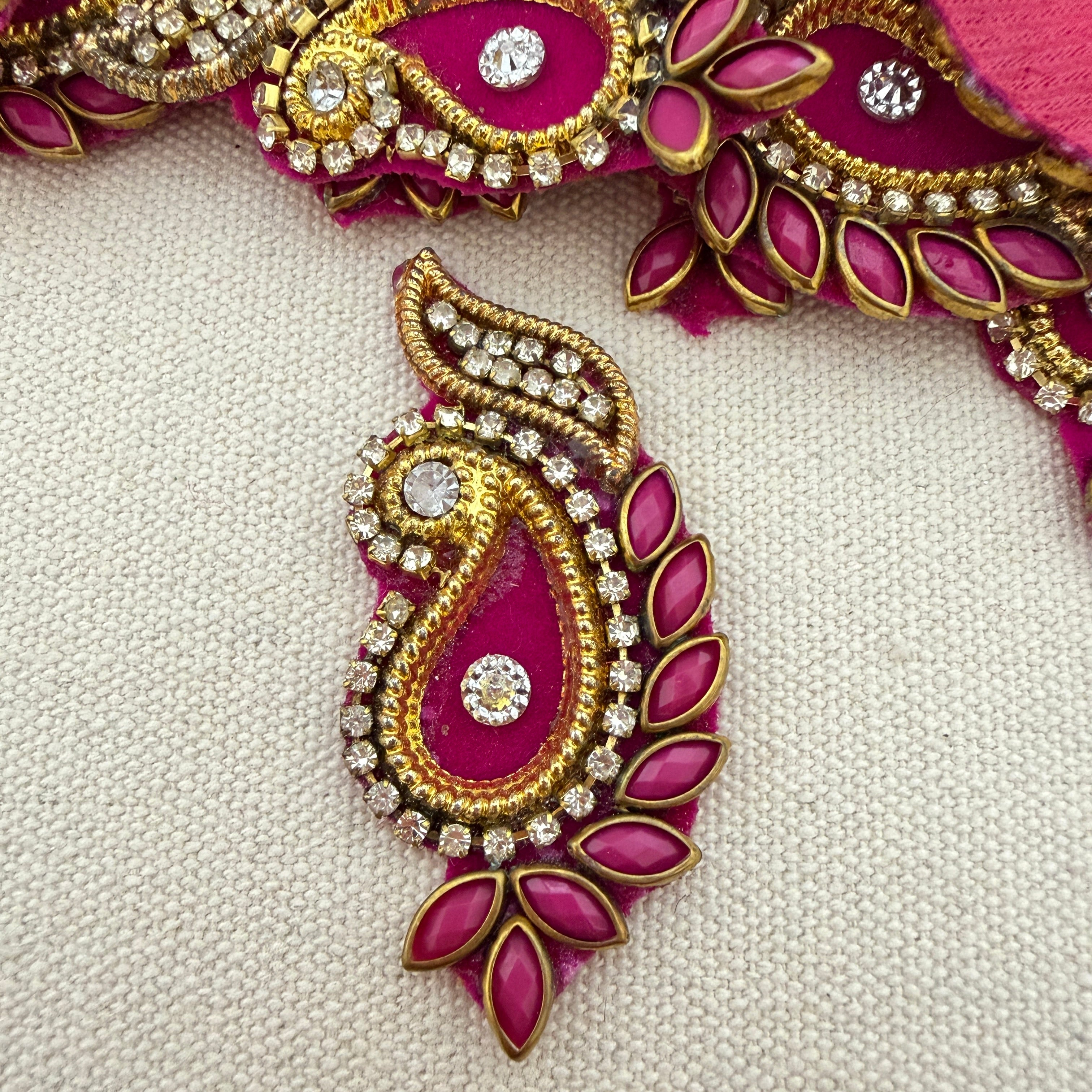 Decorative pink and gold jewelry piece with gemstones on a light gray background