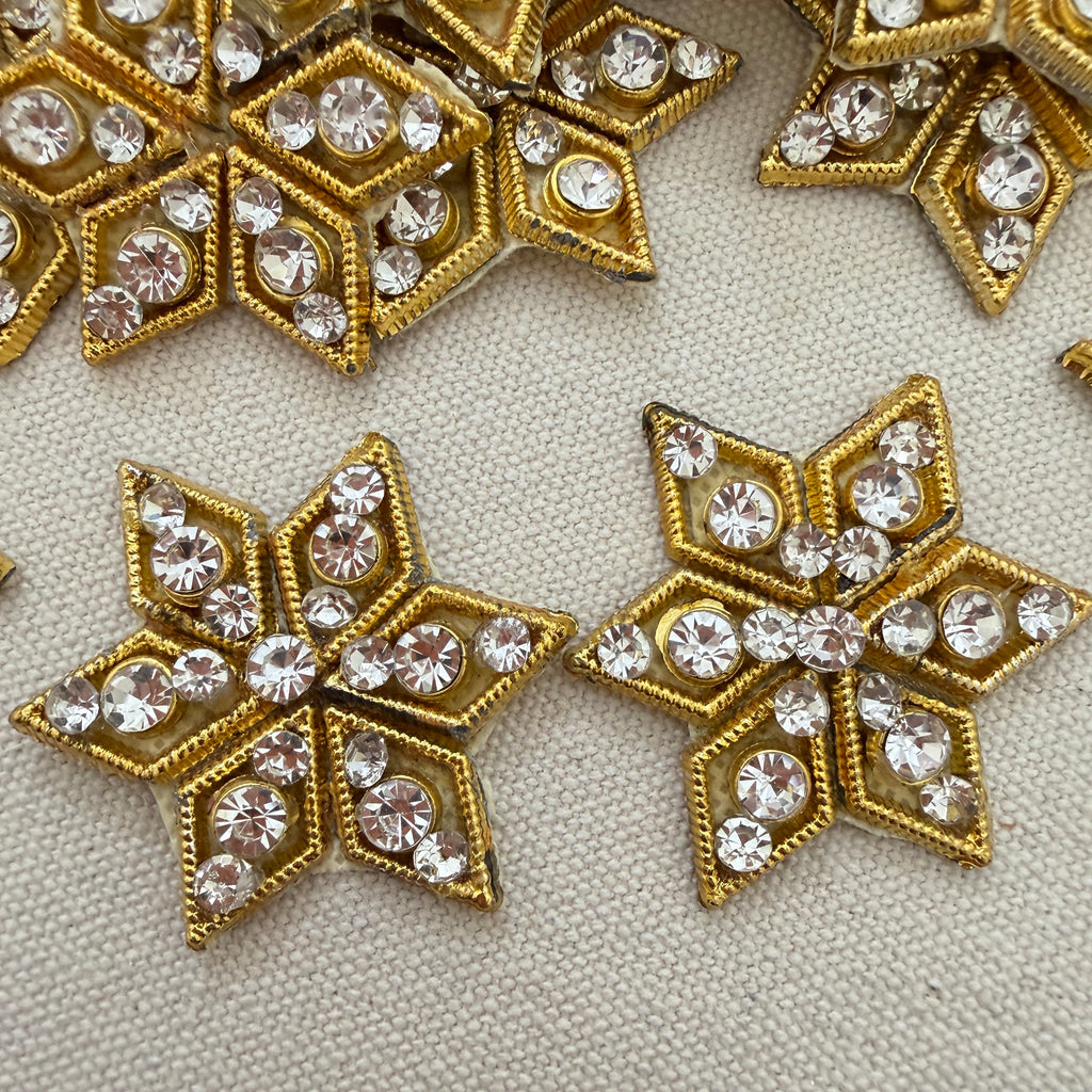 Gold star-shaped embellishments with clear rhinestones on a textured beige background