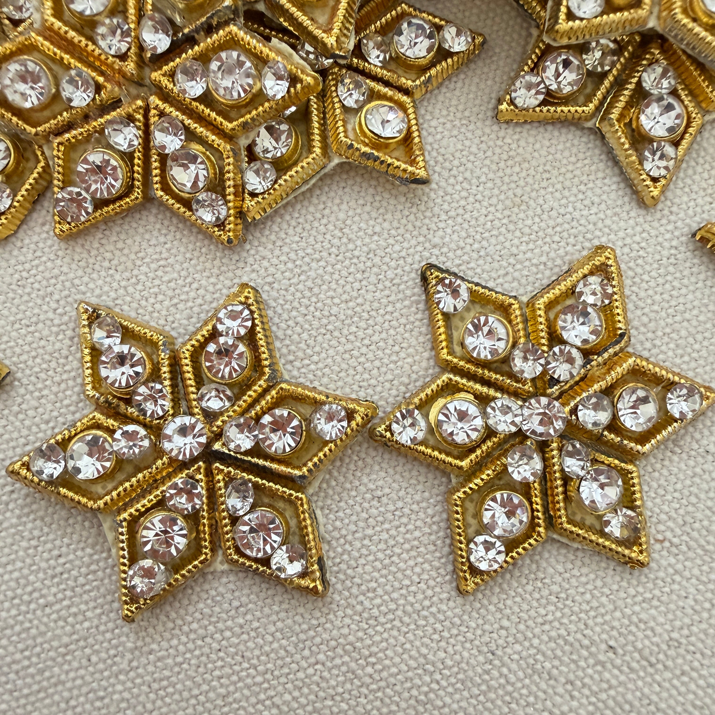 Gold star-shaped embellishments with clear rhinestones on a textured beige background