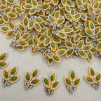 Decorative leaf-shaped embellishments with green and gold colors on a beige background.