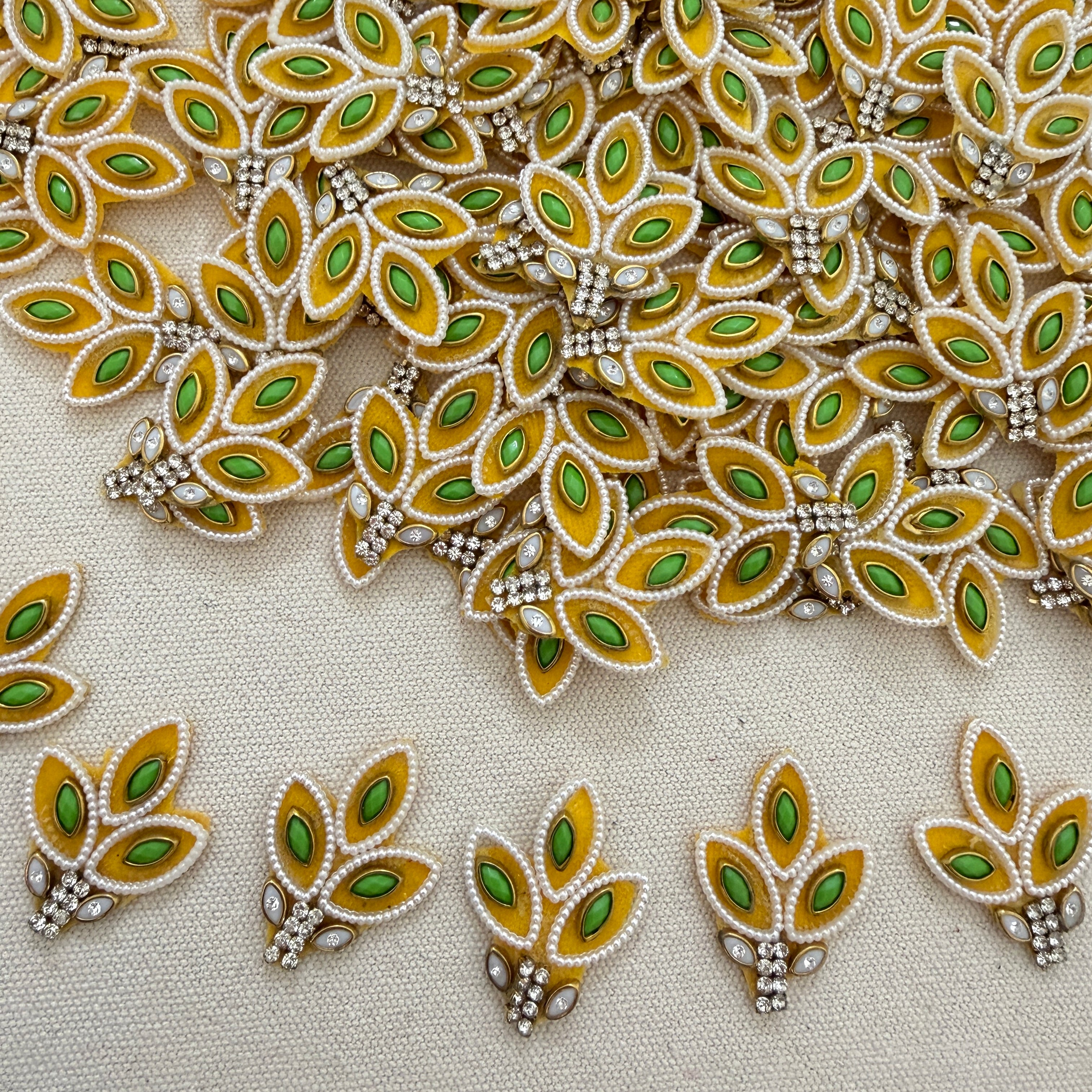 Decorative leaf-shaped embellishments with green and gold colors on a beige background.
