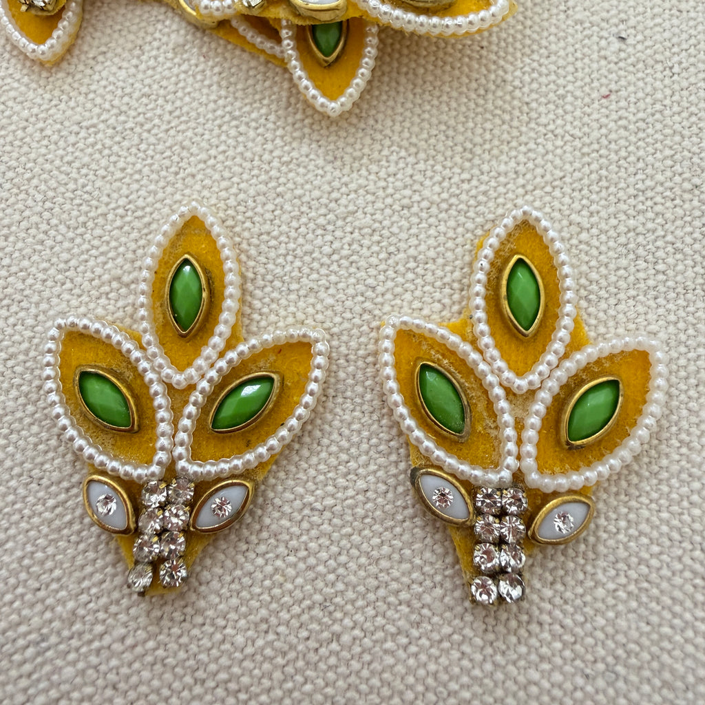 Pair of leaf-shaped earrings with green gemstones and gold accents on a textured beige background.
