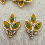 Pair of leaf-shaped earrings with green gemstones and gold accents on a textured beige background.