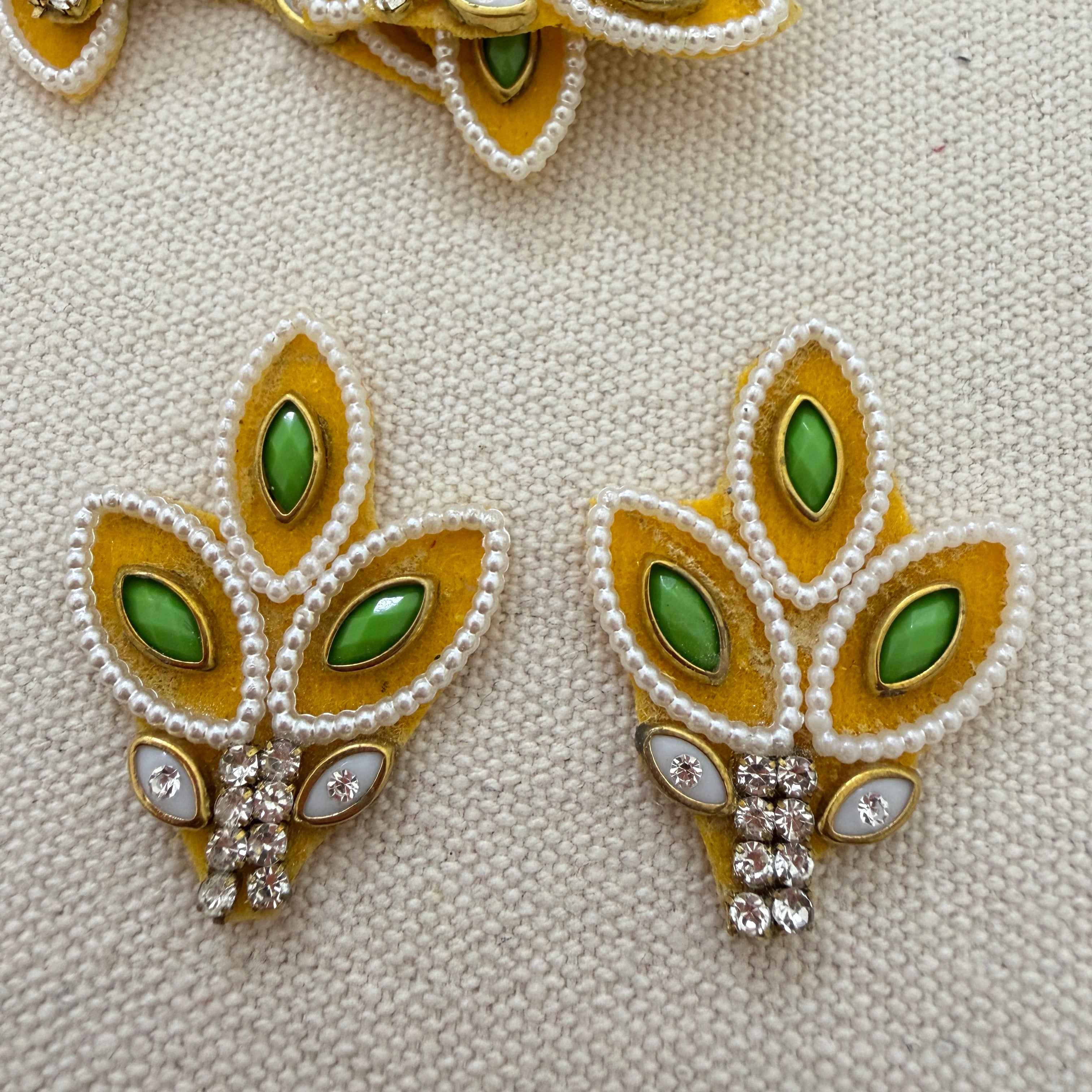 Pair of leaf-shaped earrings with green gemstones and gold accents on a textured beige background.