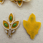 Decorative yellow brooch with green gemstones and pearl details on a textured beige background